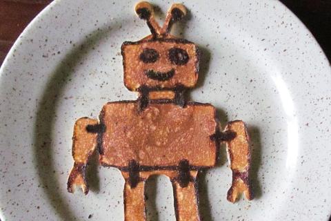 A robot-shaped pancake on a white plate. The Thai for "a robot-shaped pancake on a white plate" is "แพนเค็กรูปหุ่นยนต์บนจานสีขาว". A robot-shaped pancake on a white plate. The Thai for "a robot-shaped pancake on a white plate" is "แพนเค็กรูปหุ่นยนต์บนจานสีขาว".