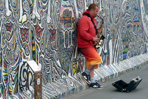 A man is playing the saxophone by the roadside. The Thai for "a man is playing the saxophone by the roadside" is "ผู้ชายเป่าแซ็กโซโฟนข้างทาง".
